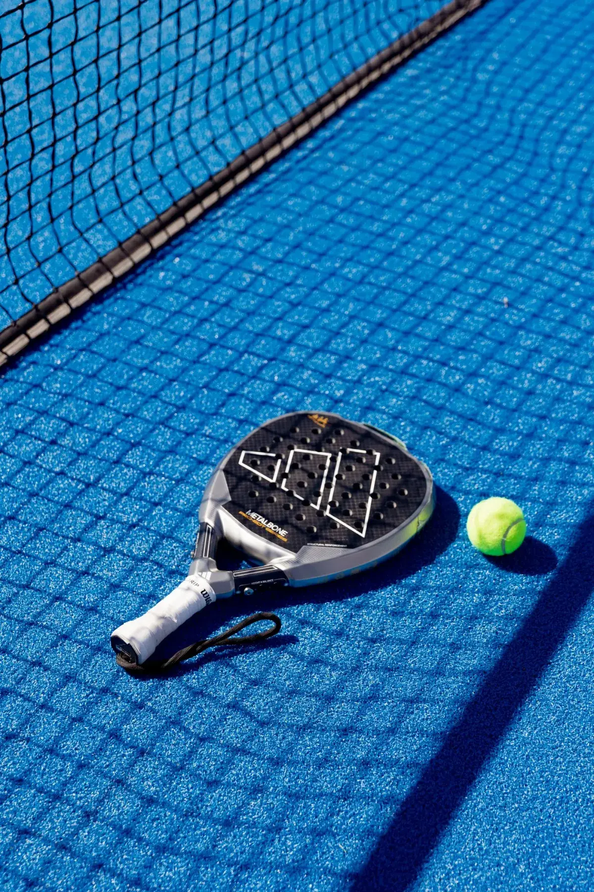 Padel racket and ball resting on the court, next to the net